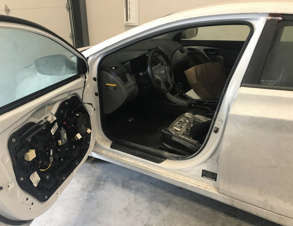 Open car driver door with inner trim removed, exposed mechanisms and partly stripped seat.