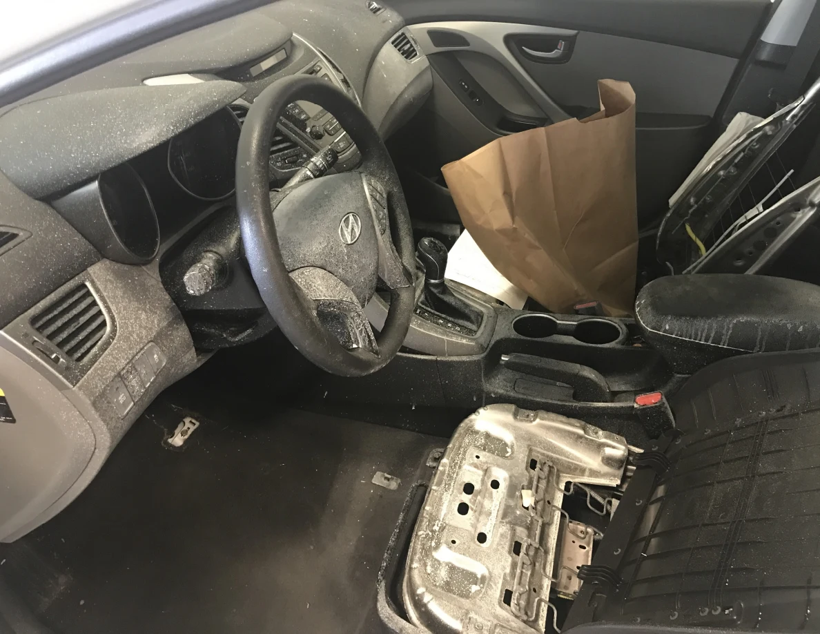 Car interior with steering wheel, exposed seat components and paper bags.