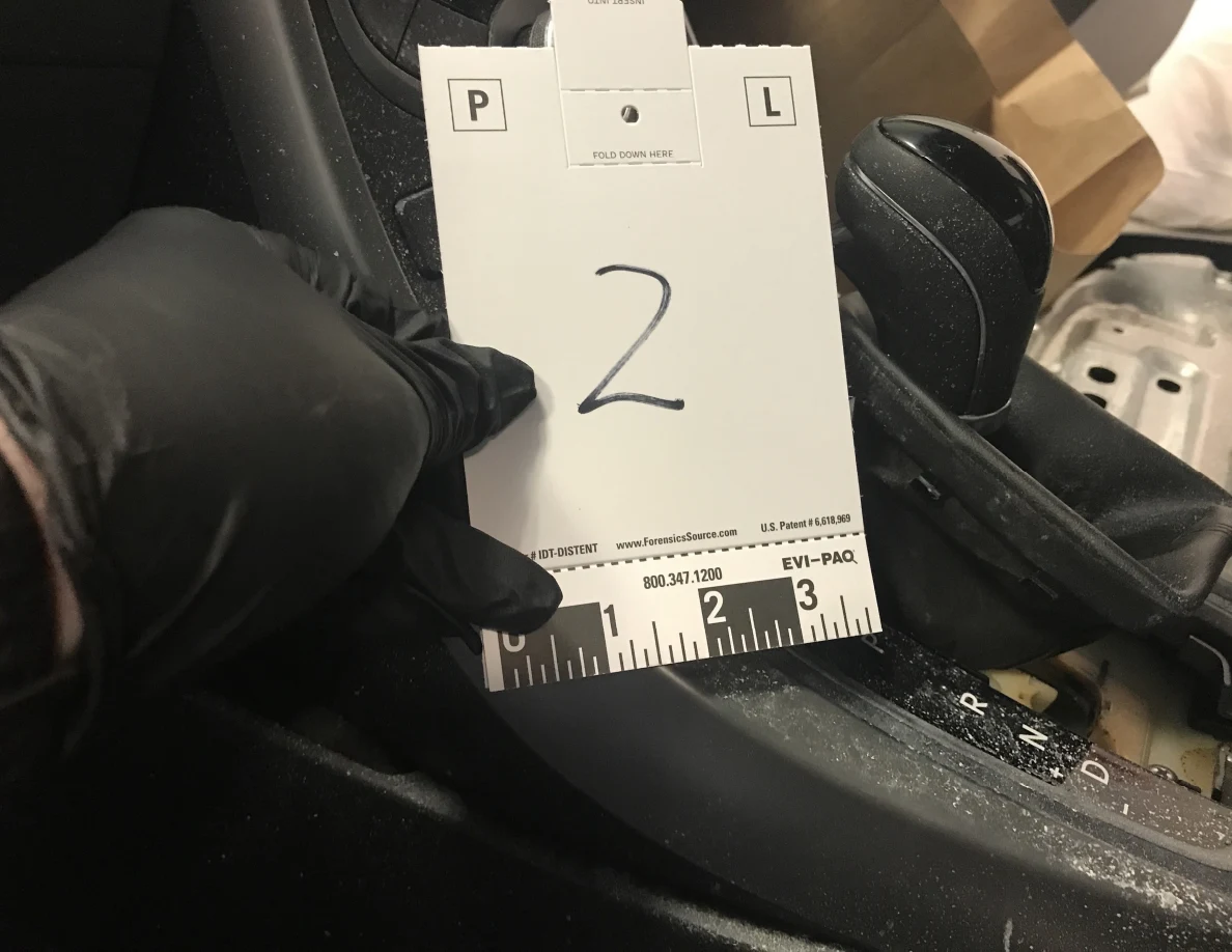 Gloved hand holding reference card 2 beside car gear selector and center console.