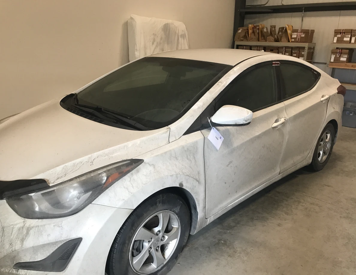 Front and side of white sedan with paper tag near side mirror indoors.