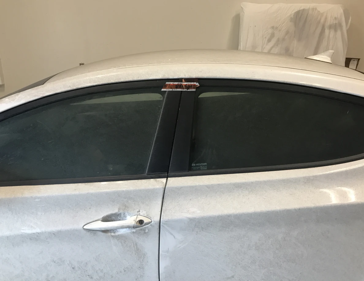 White car side windows and doors with tape near upper frame.