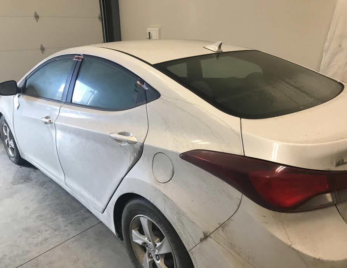 Rear quarter of white sedan and fuel door indoors.