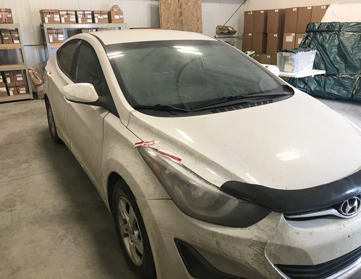 Front quarter of white sedan with windshield and headlight visible indoors.