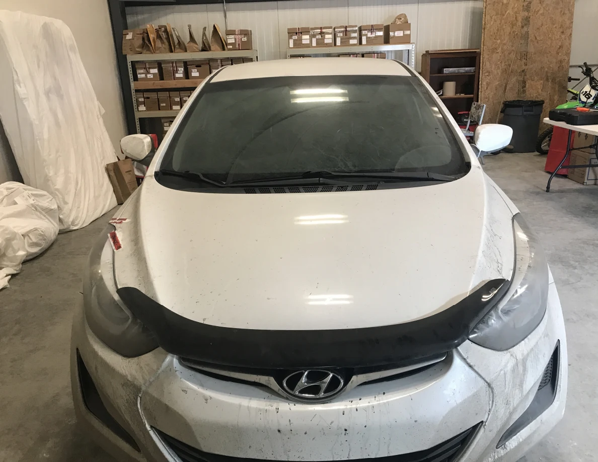 Front of white sedan with windshield and hood visible indoors.