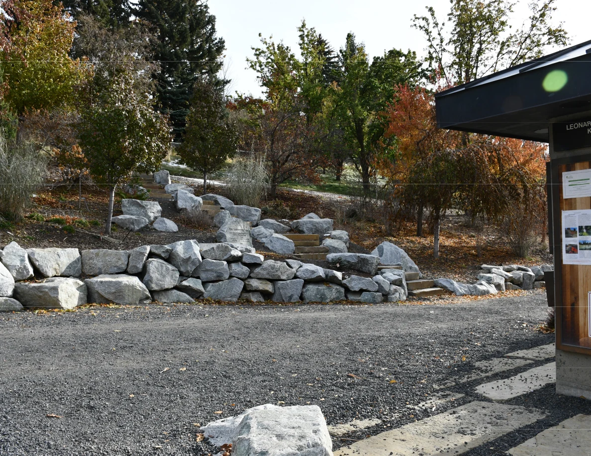 Landscaped outdoor stone steps and a low rock wall beside a gravel path, trees and the edge of an information shelter.