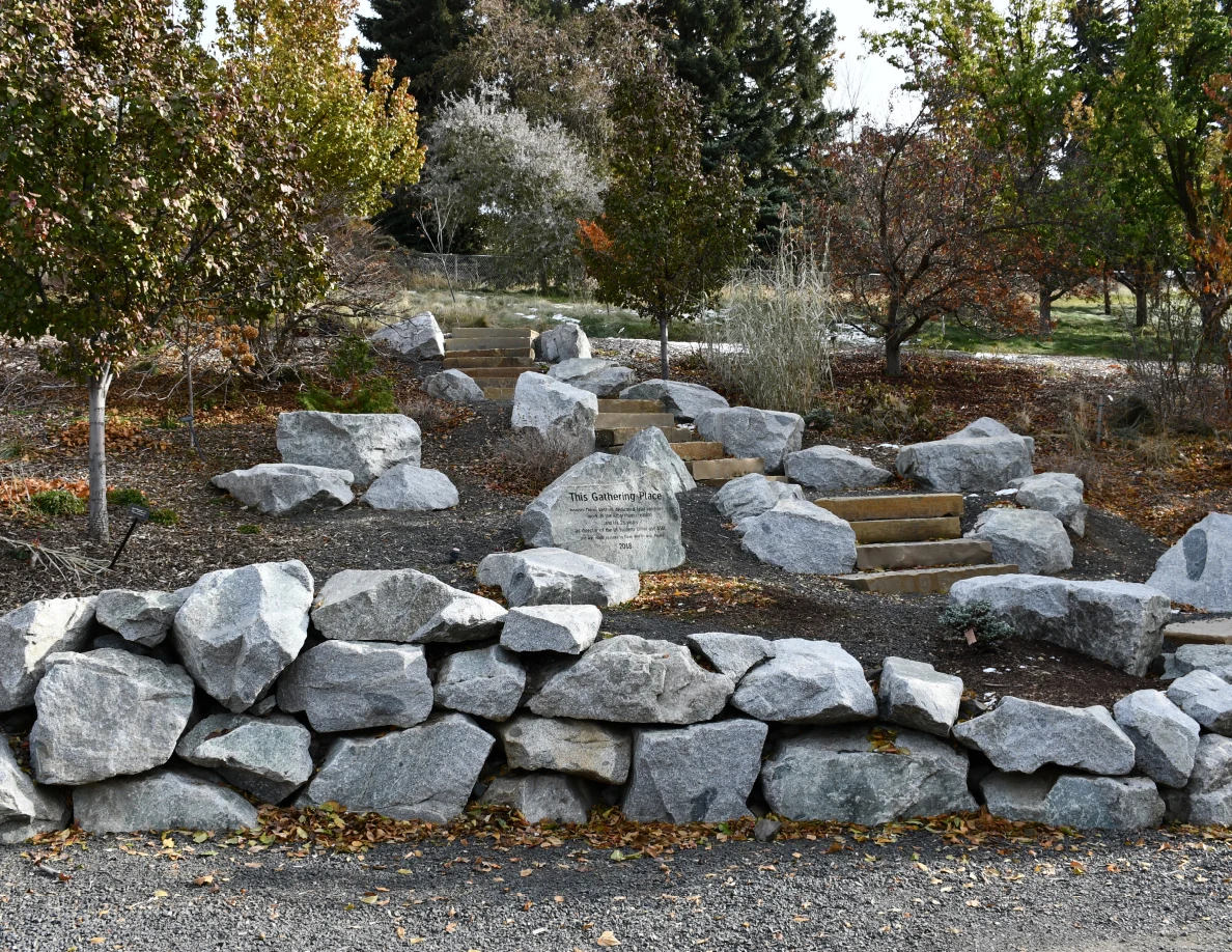 Stone steps rising through landscaping rocks and autumn trees behind a low stacked-rock wall.