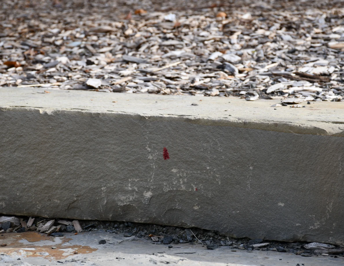 Close view of a small reddish triangular mark on a vertical stone stair face.