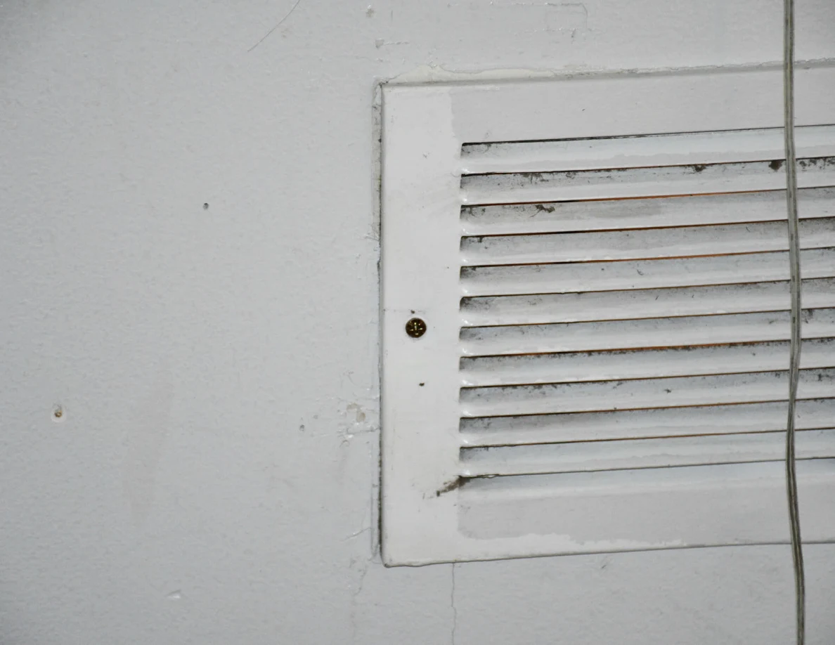 Close view of the left side of a white slatted wall ventilation grille and a hanging cord.