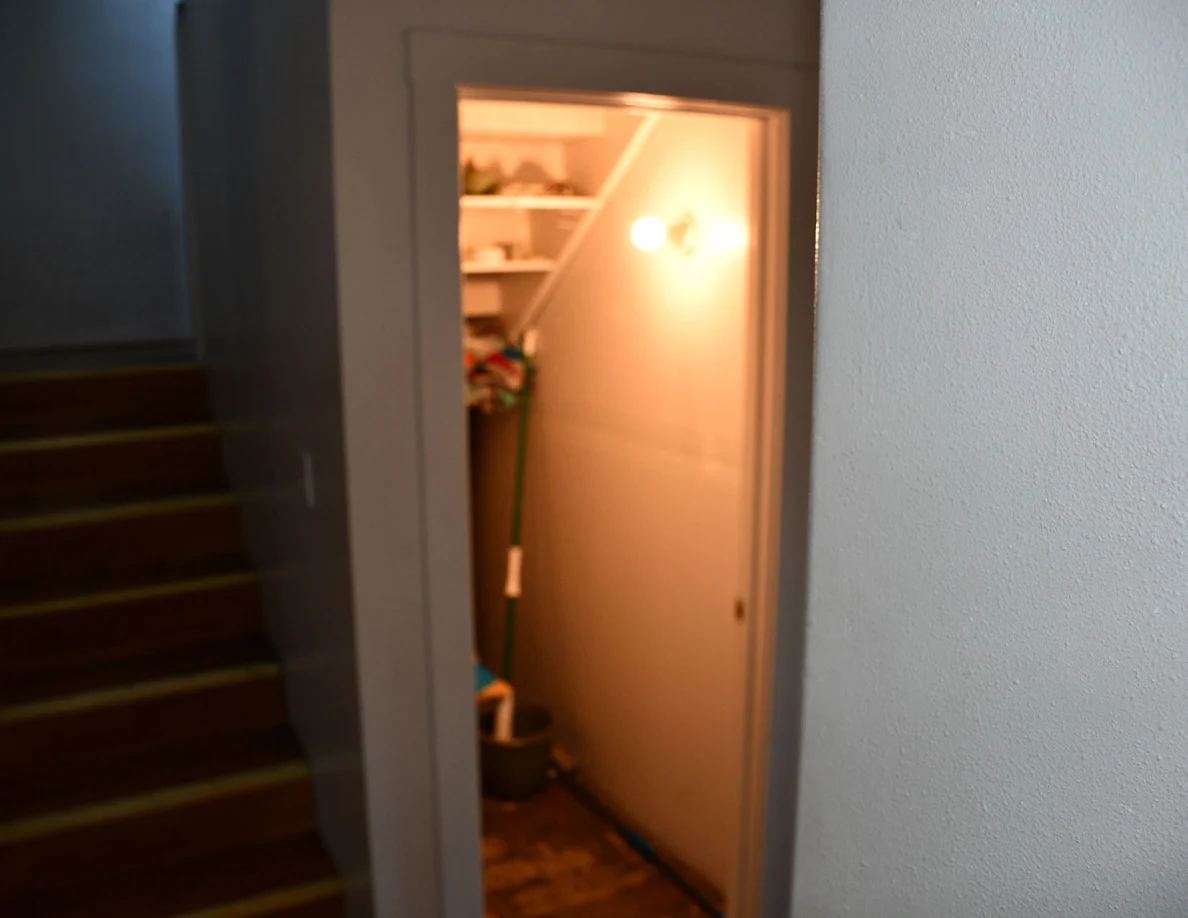 Open illuminated storage closet with shelves beside an indoor wooden staircase.