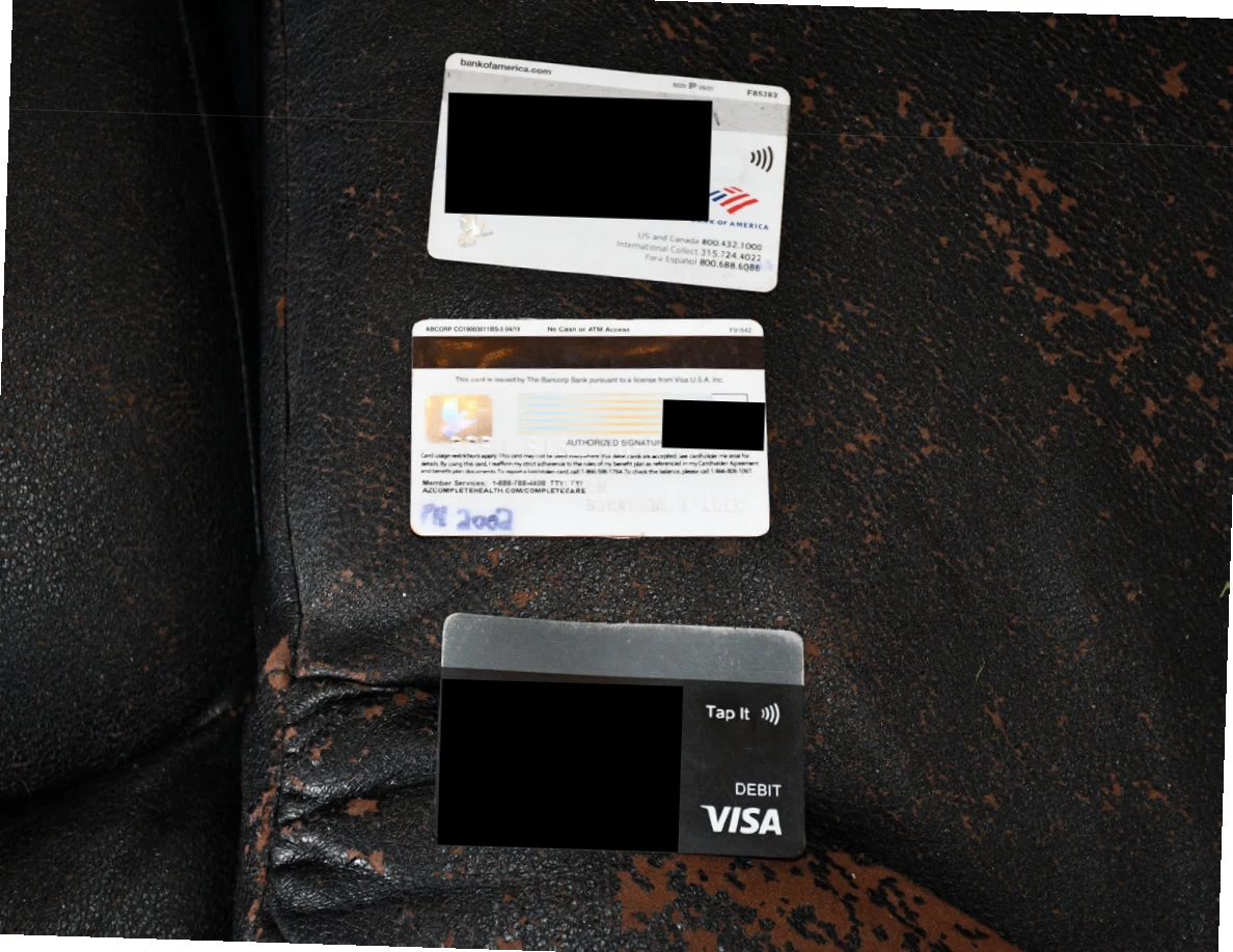 Three cards on black upholstery, including debit-card branding, with large black redactions over personal details.
