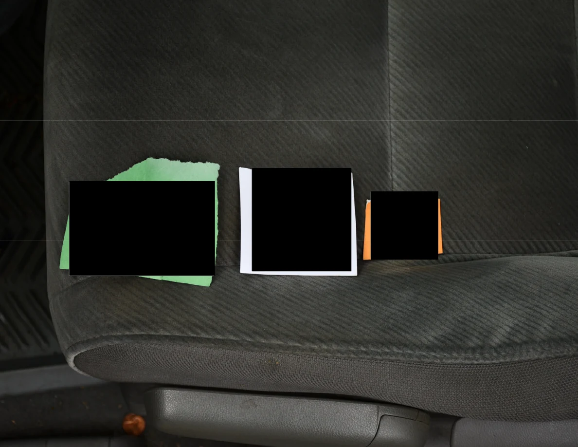 Three small papers or cards on a gray vehicle seat, mostly covered by black redactions.