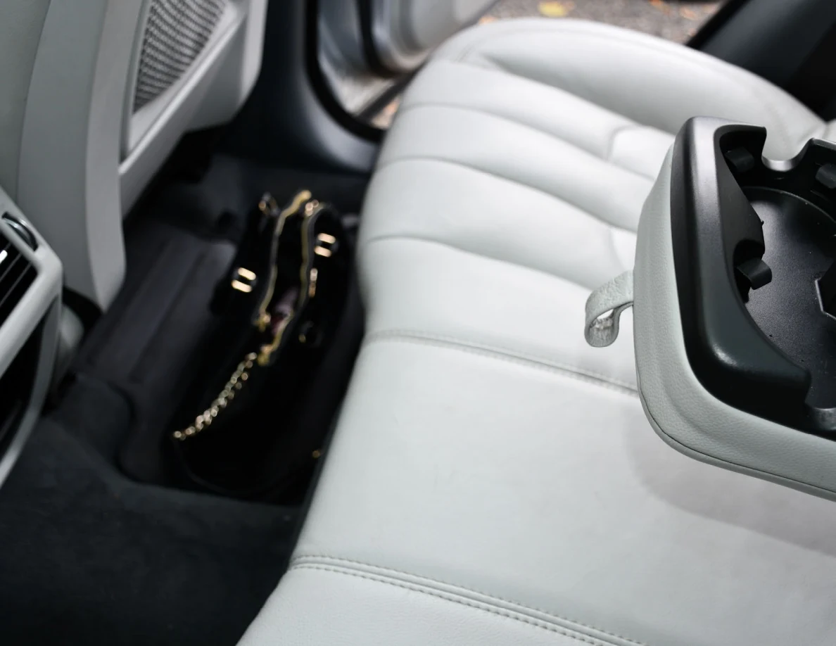 White leather vehicle rear seat with a lowered cup-holder armrest and a black handbag in the footwell.