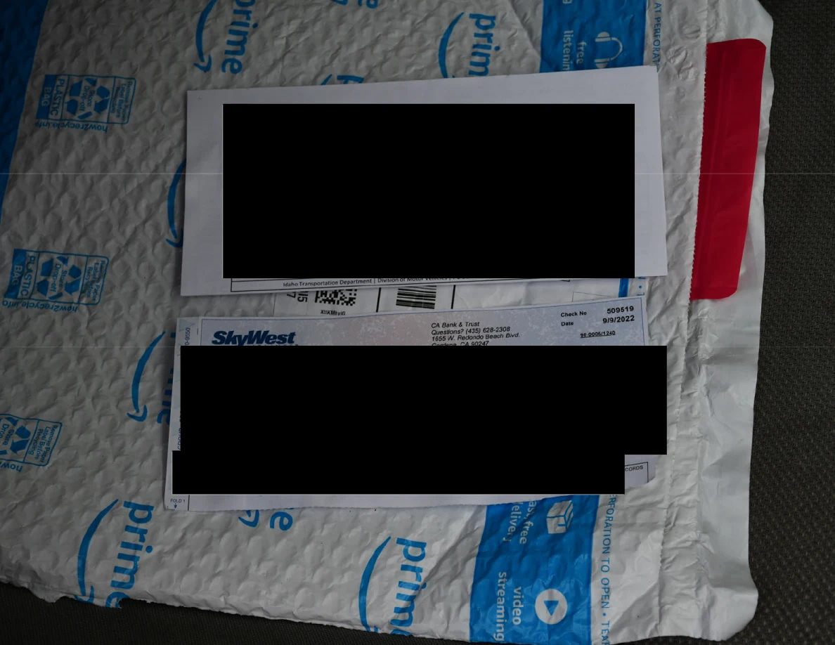 Two paper items resting on an Amazon padded mailer, with identifying details covered by large black redactions.
