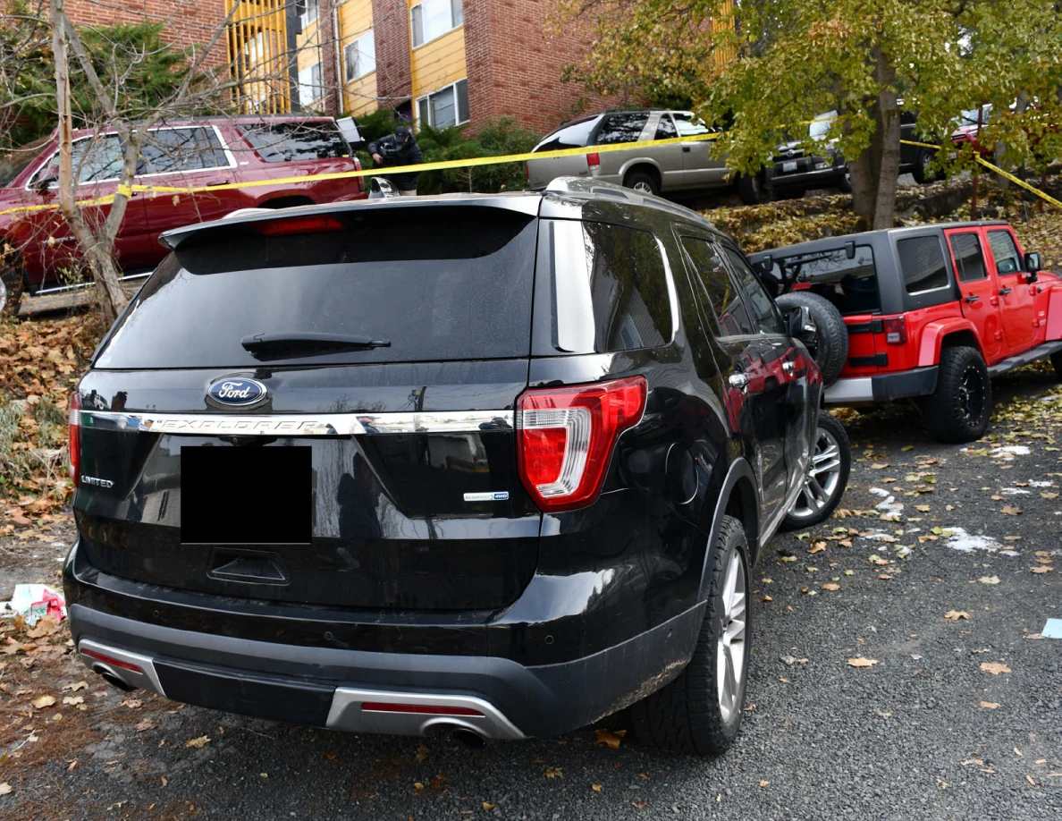 Rear of a black Ford SUV beside a red Jeep, with yellow tape and other parked vehicles behind.
