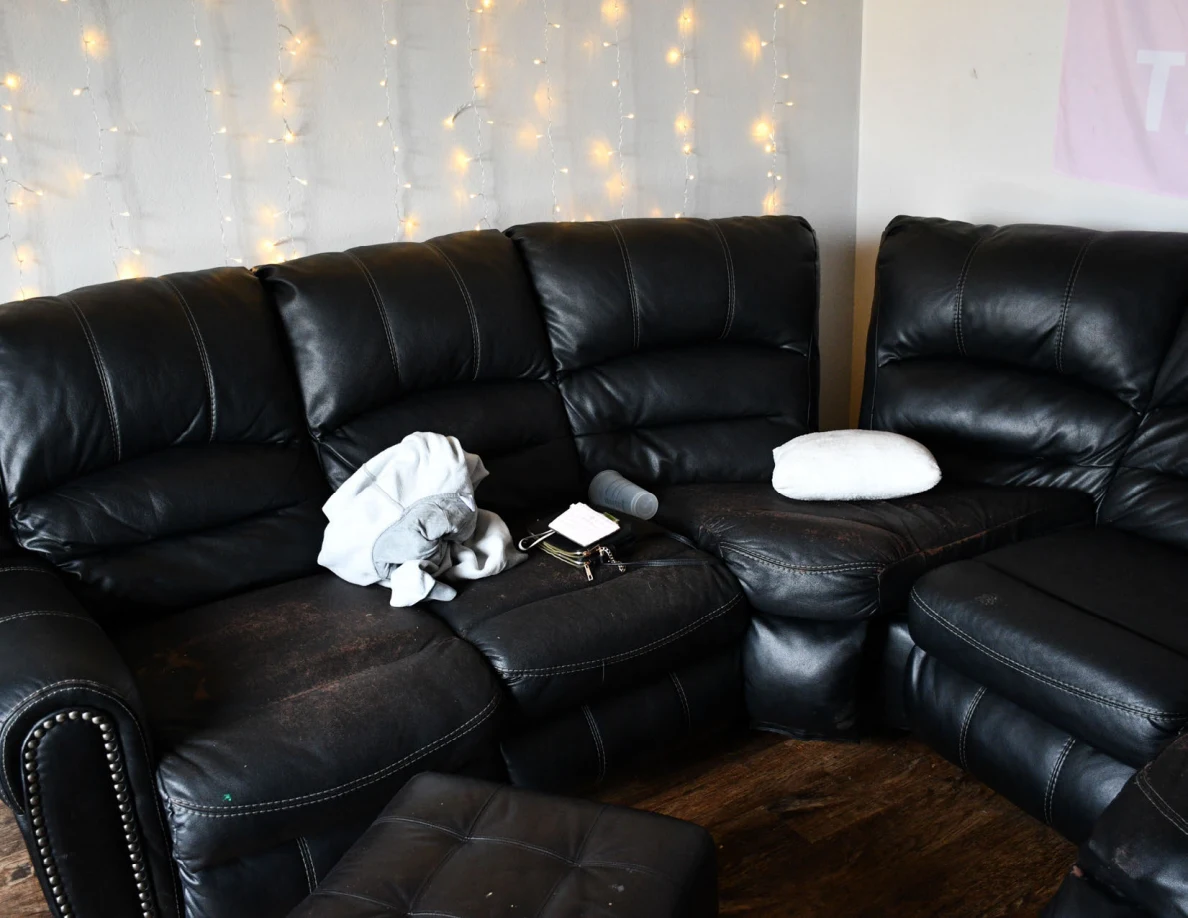 Black leather sectional seating with a white pillow, loose blanket, cups and small papers beneath string lights.