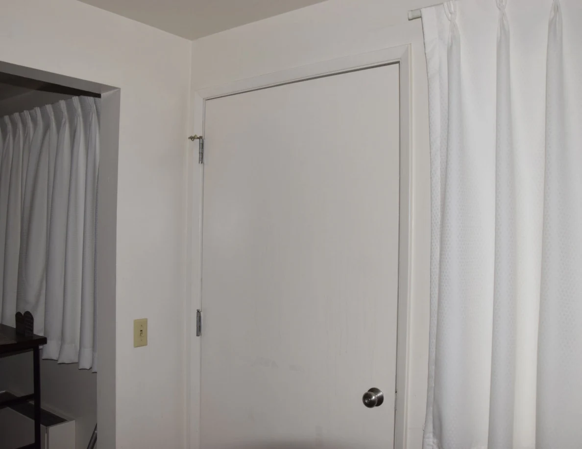 Upper view of a closed white door beside white curtains and an open alcove.