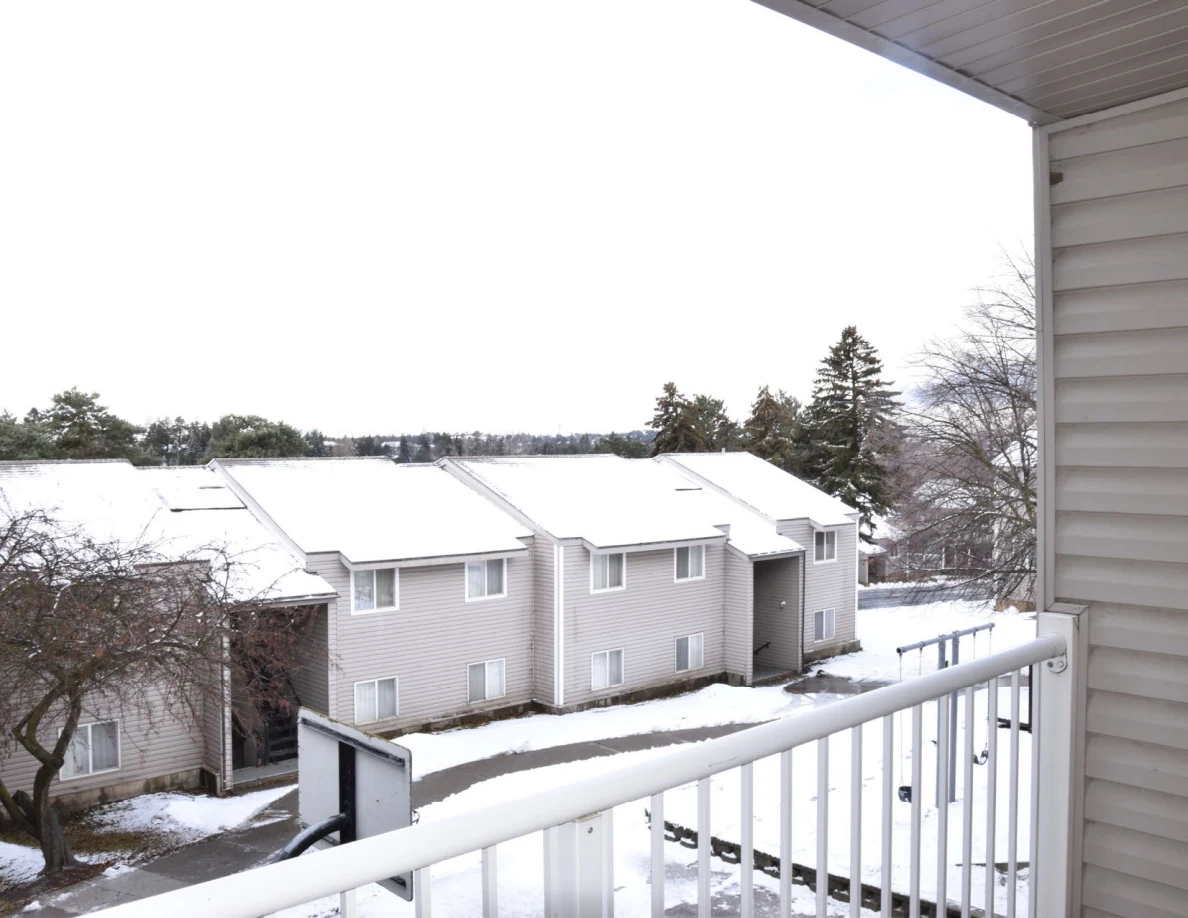 View from a covered balcony across white railings toward snow-covered residential buildings.
