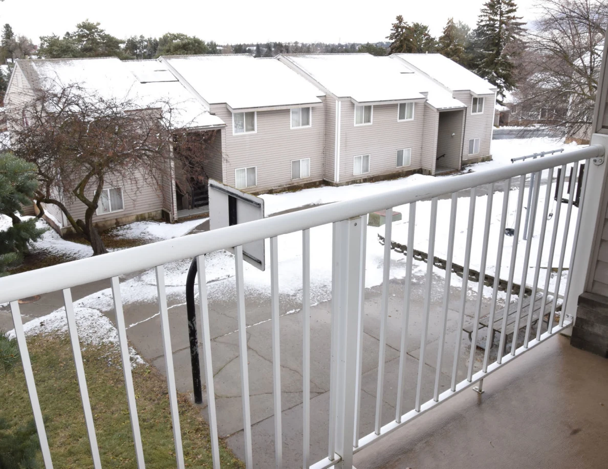 Snow-covered residential buildings and a road viewed over a white balcony railing.