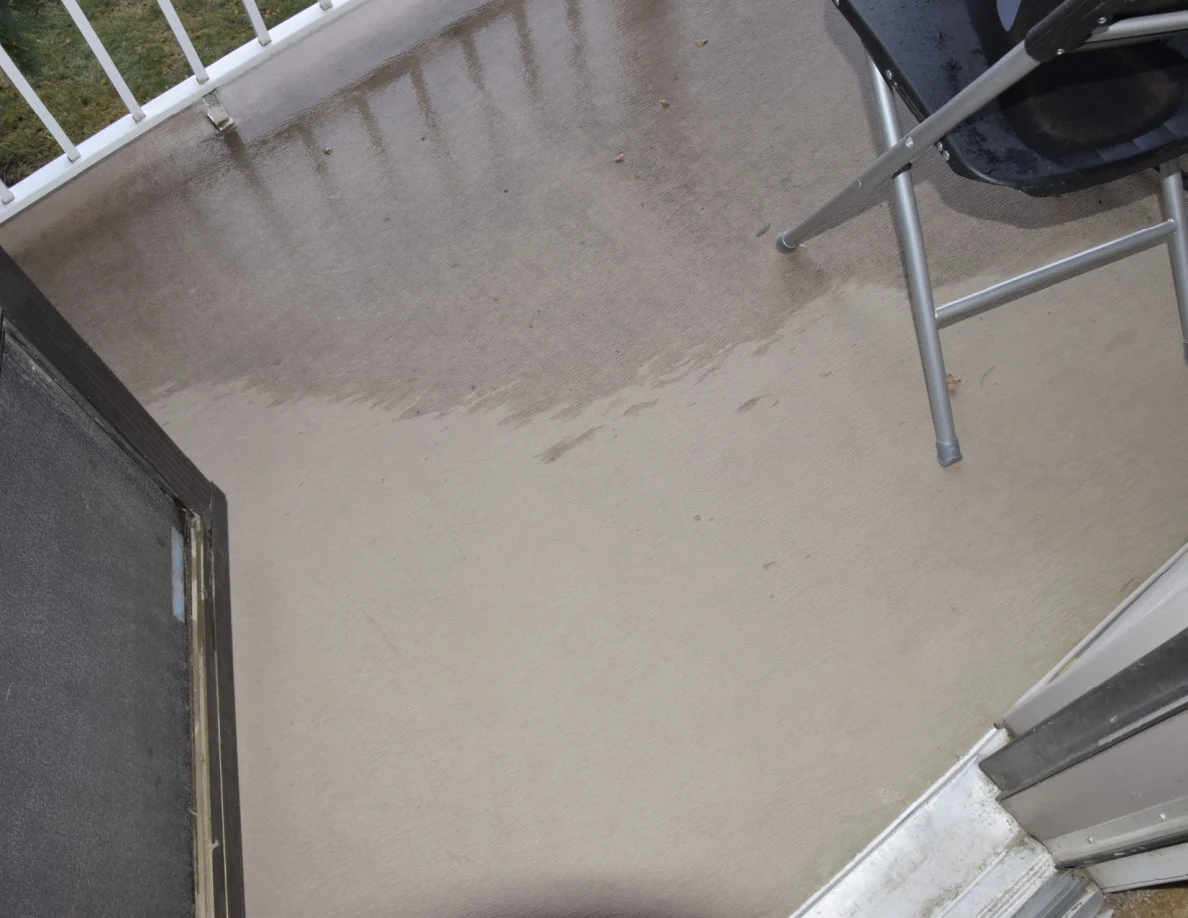 Wet balcony floor beside an open storm door and the legs of a folding chair.