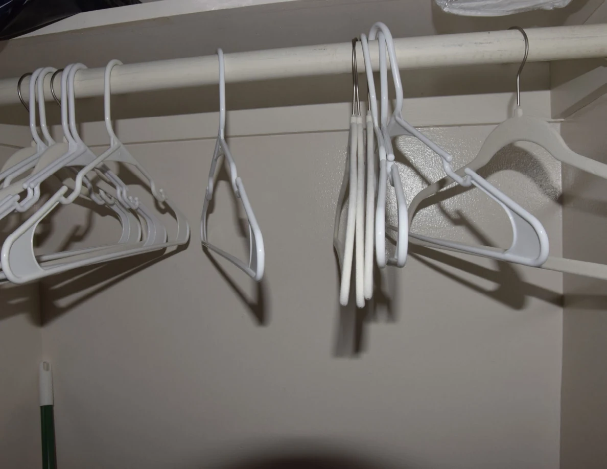 White plastic hangers on a closet rod beneath a shelf.