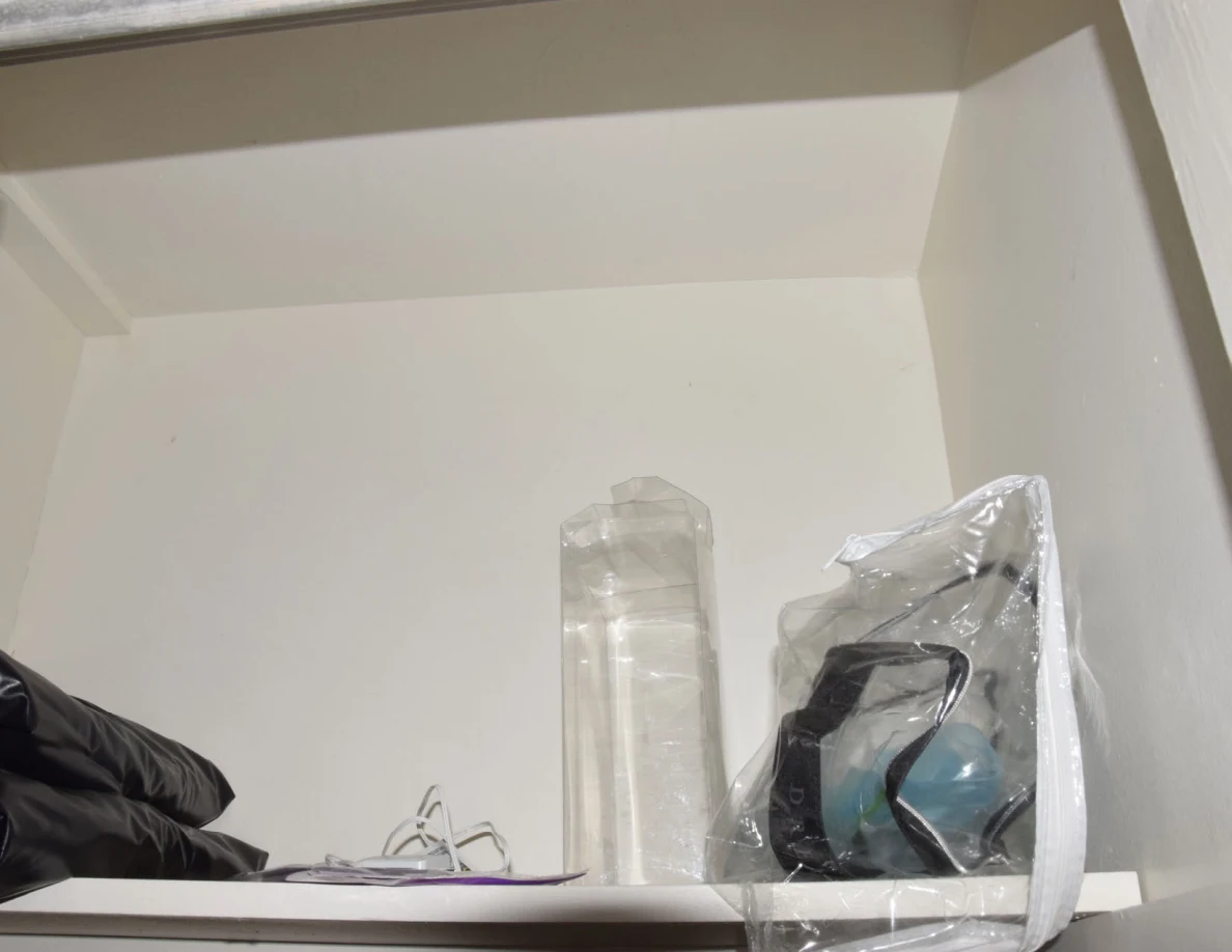 Upper closet shelf holding clear packaging, a dark item and a plastic-wrapped household appliance.