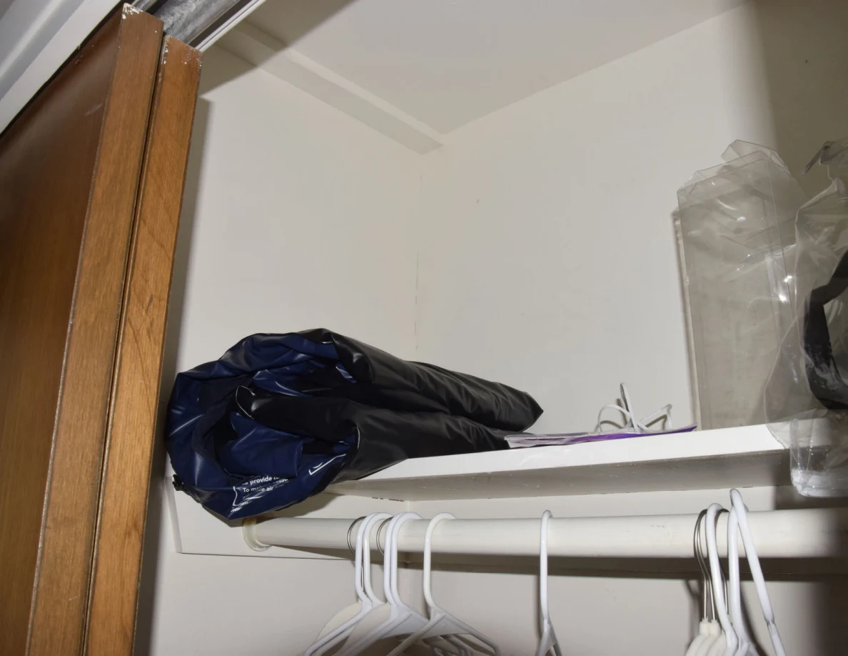 Upper closet shelf with dark folded material and clear packaging, above empty white hangers.