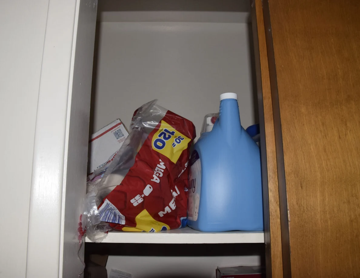 Closet shelf with a large red paper-product package and blue detergent containers.