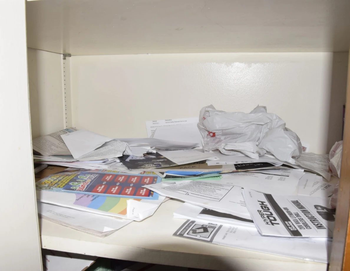 Loose papers, envelopes, booklets and plastic bags spread across a white shelf.