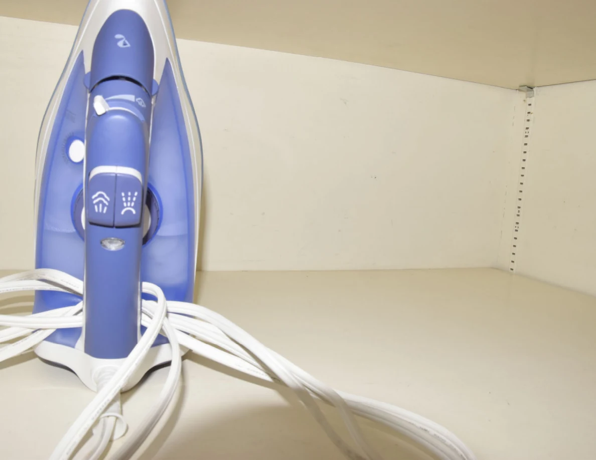 Close view of a blue-and-white clothes iron and its cord on a storage shelf.