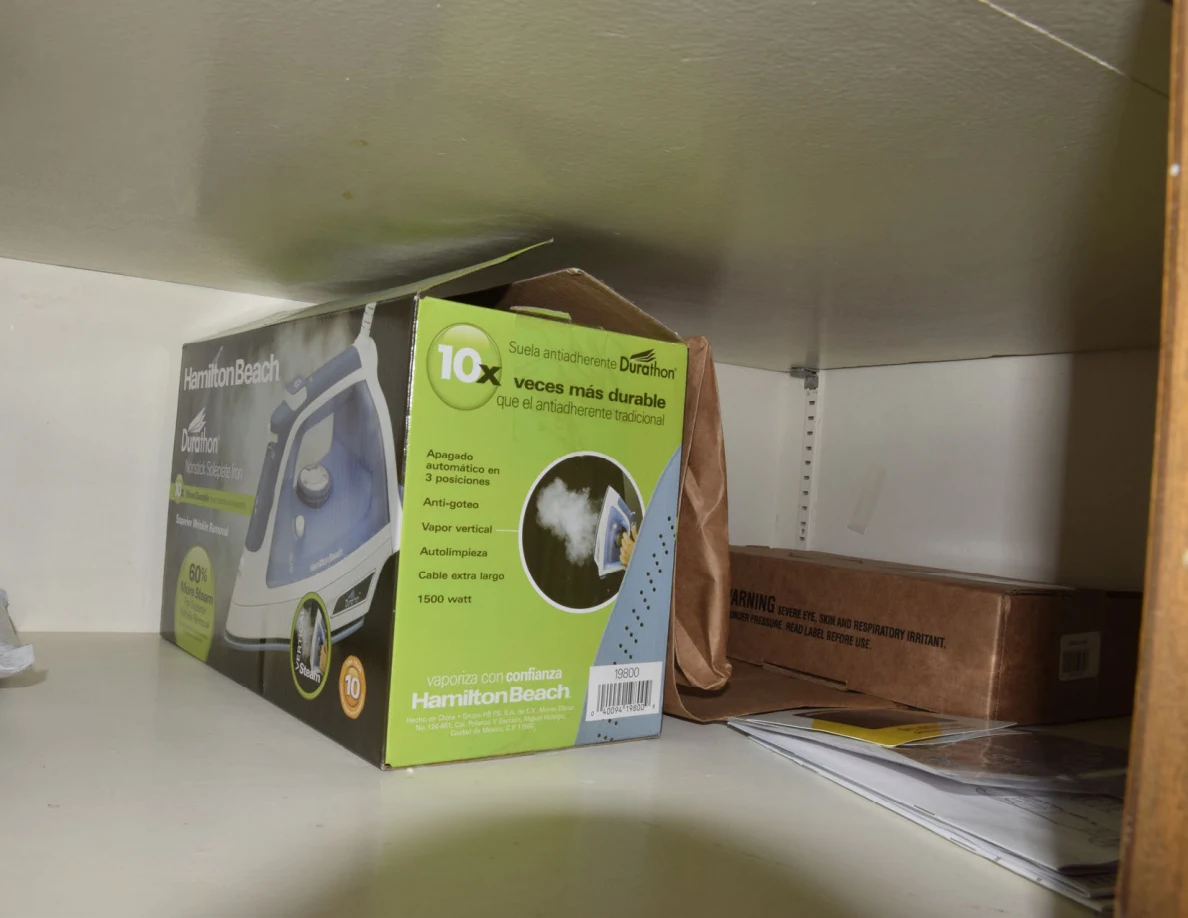 Clothes-iron retail box beside a paper bag, cardboard box and papers on a shelf.