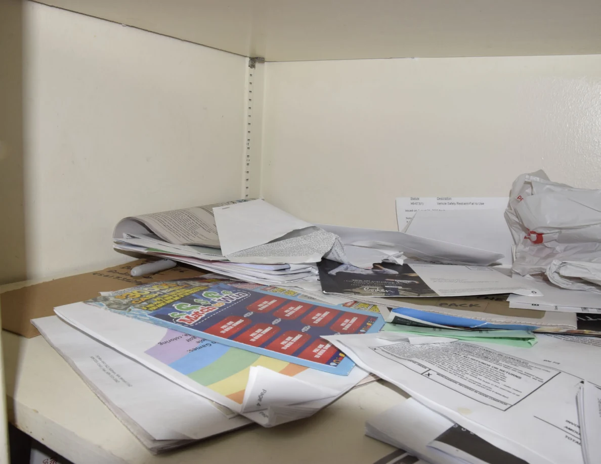 Close view of loose papers, envelopes and colorful booklets piled on a white shelf.