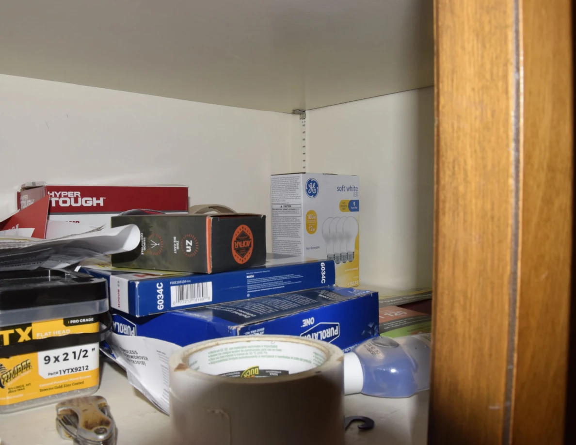Small hardware and light-bulb boxes beside a roll of white tape and other supplies on a shelf.