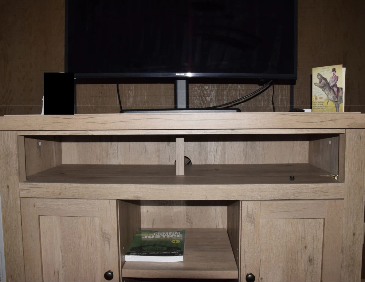 Television on a wooden media cabinet, with open shelves, a book and a standing greeting card.