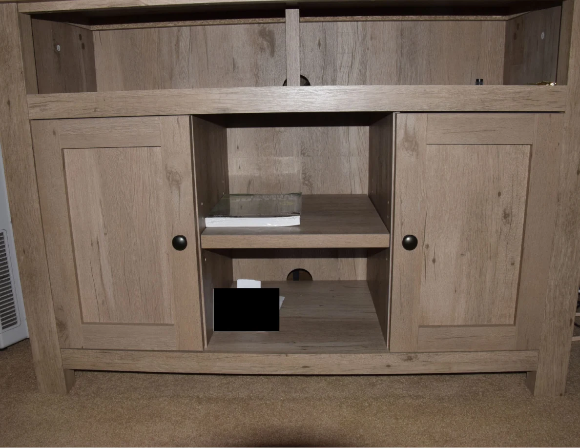 Wooden media cabinet with closed side doors, open center shelves and a small black redaction.
