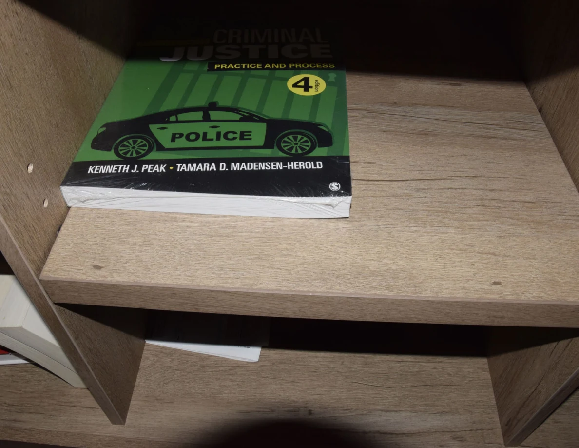 Green Criminal Justice: Practice and Process textbook on a wooden shelf, with a police-car illustration on its cover.