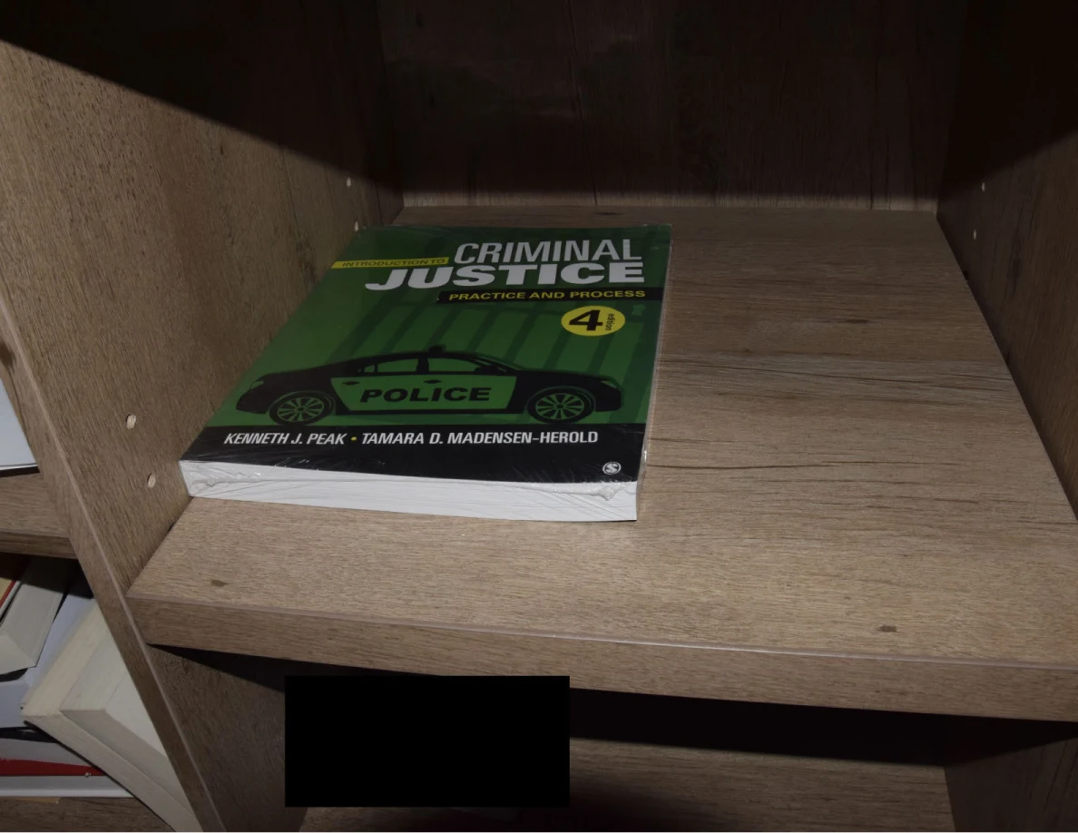 Angled view of a green criminal-justice textbook on a wooden shelf, with a black redaction below.