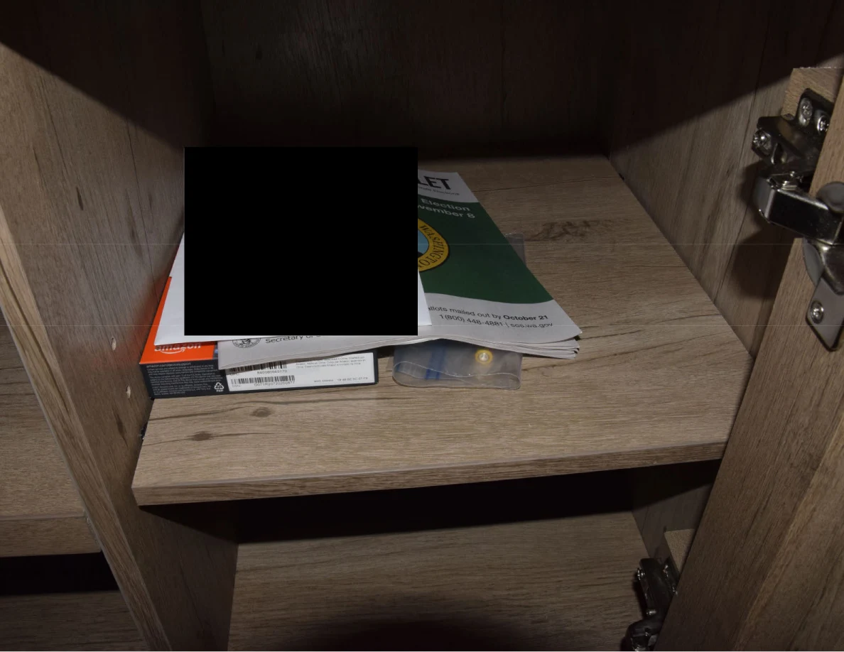 Small stack of booklets and boxes in a wooden cabinet compartment, largely obscured by a black redaction.