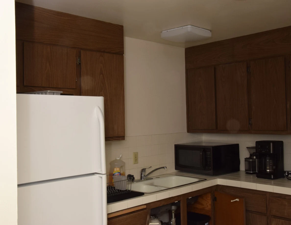 Kitchen with wood cabinets, white refrigerator, sink, microwave and coffee maker, with lower cabinet doors open.