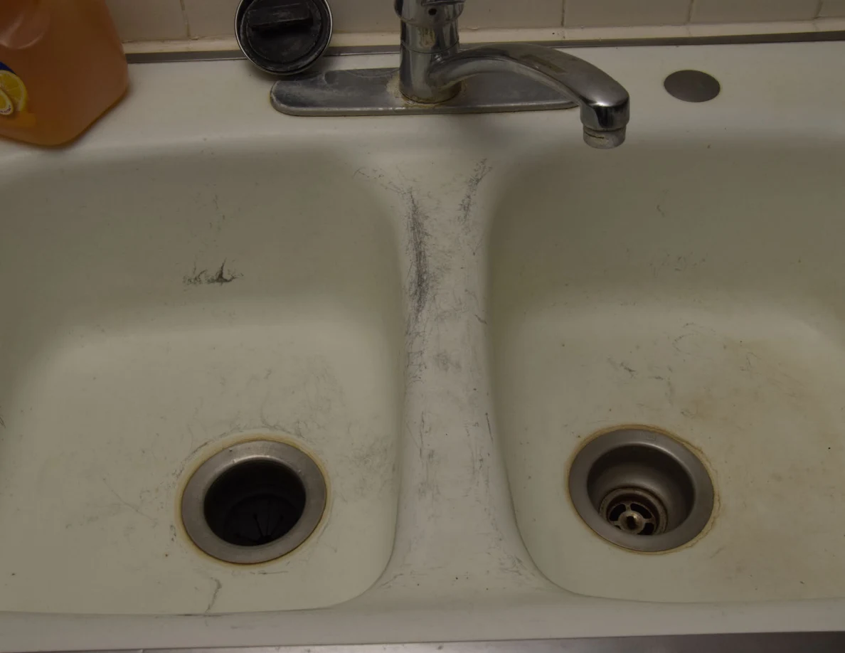 Close view of a white double-basin kitchen sink with dark scuff marks and metal faucet.