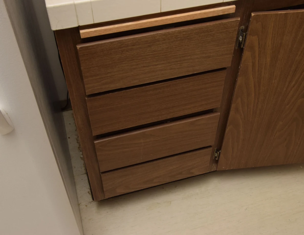 Four closed wooden kitchen drawers beside an open cabinet door.