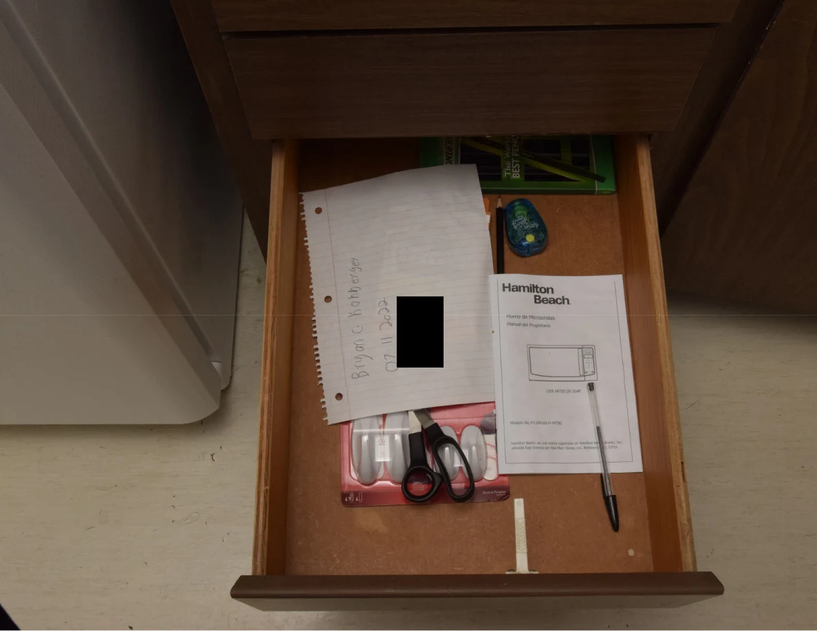 Open drawer with papers, scissors, a pen and appliance instructions, with a small black redaction.