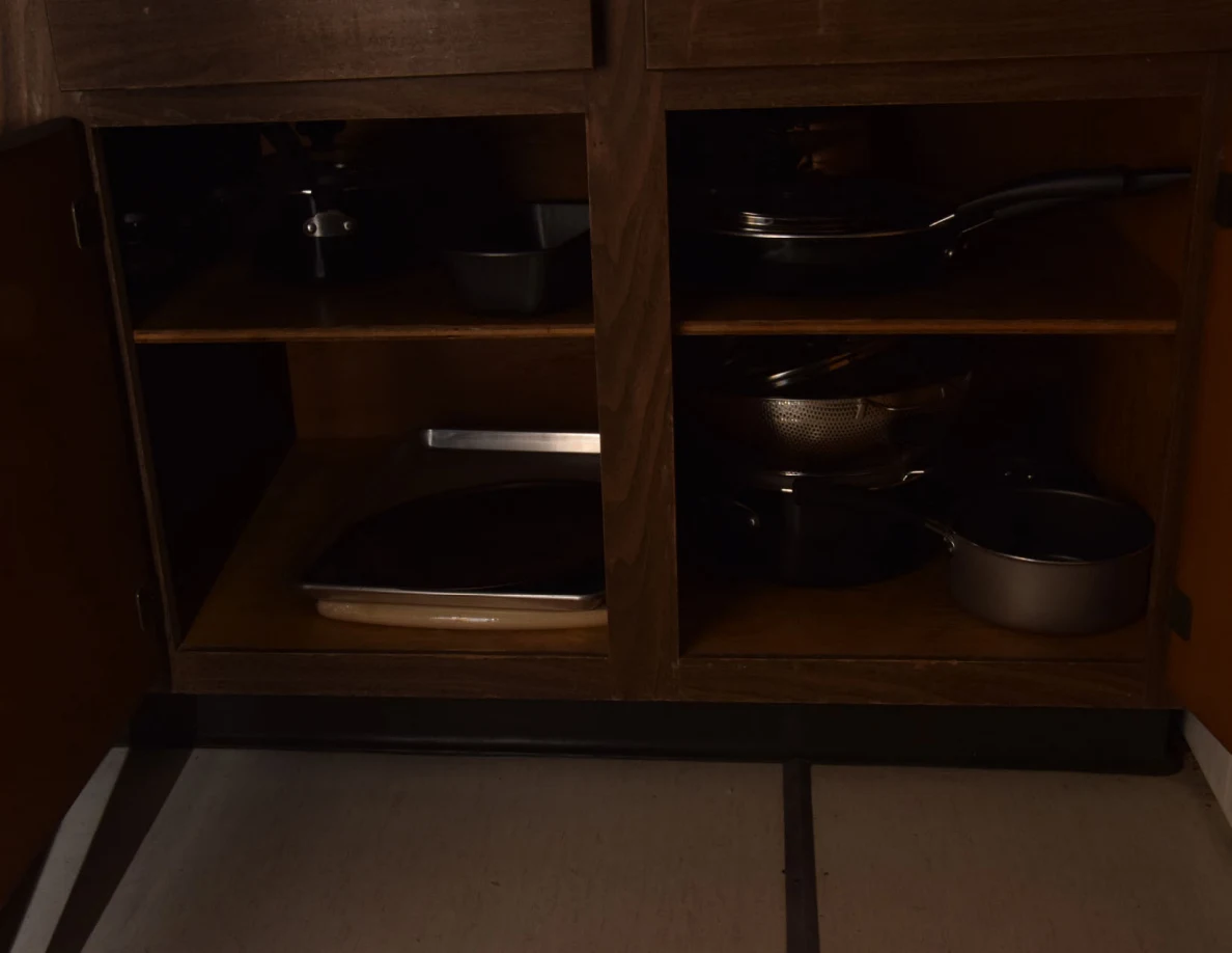 Dim view inside an open cabinet containing cookware and baking trays.