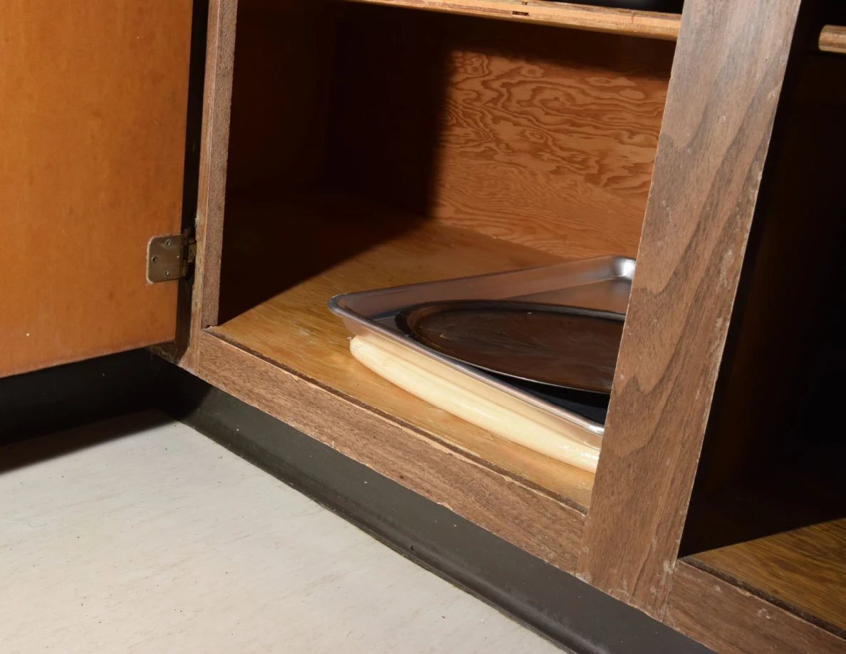 Lower cabinet shelf holding baking trays and a round pan or tray on a cutting board.