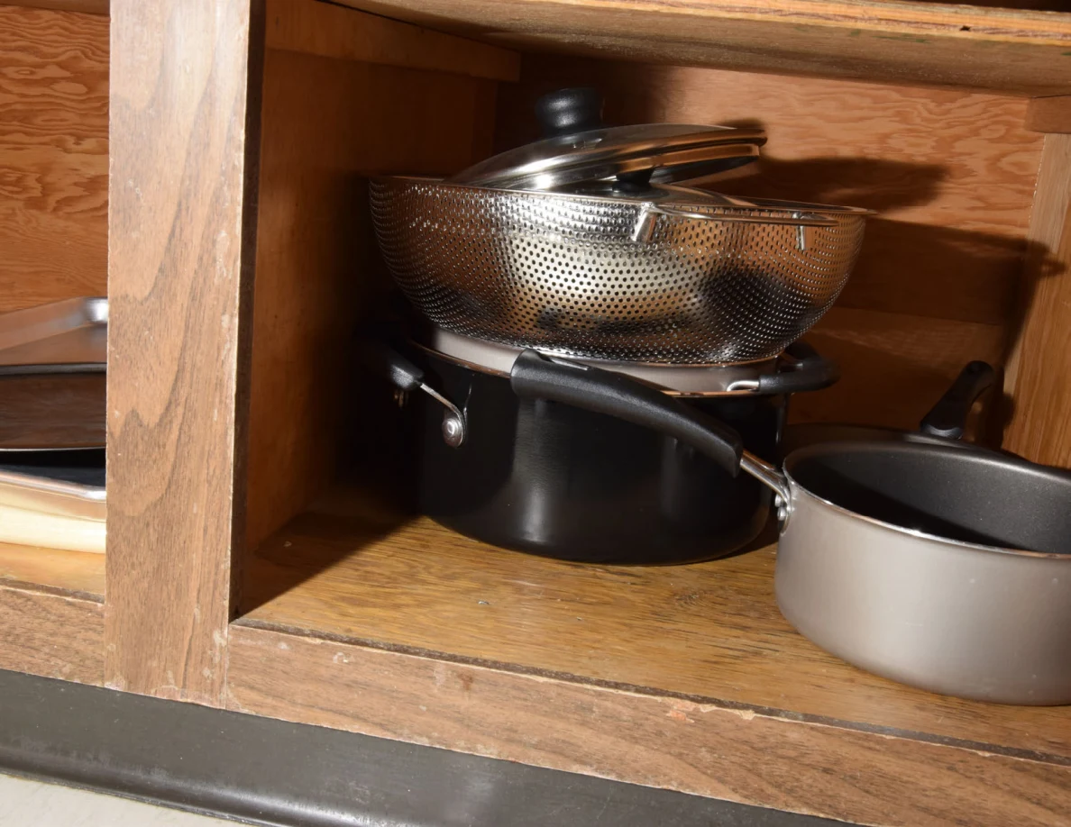 Colander and lids stacked over a black cooking pot beside a gray saucepan.