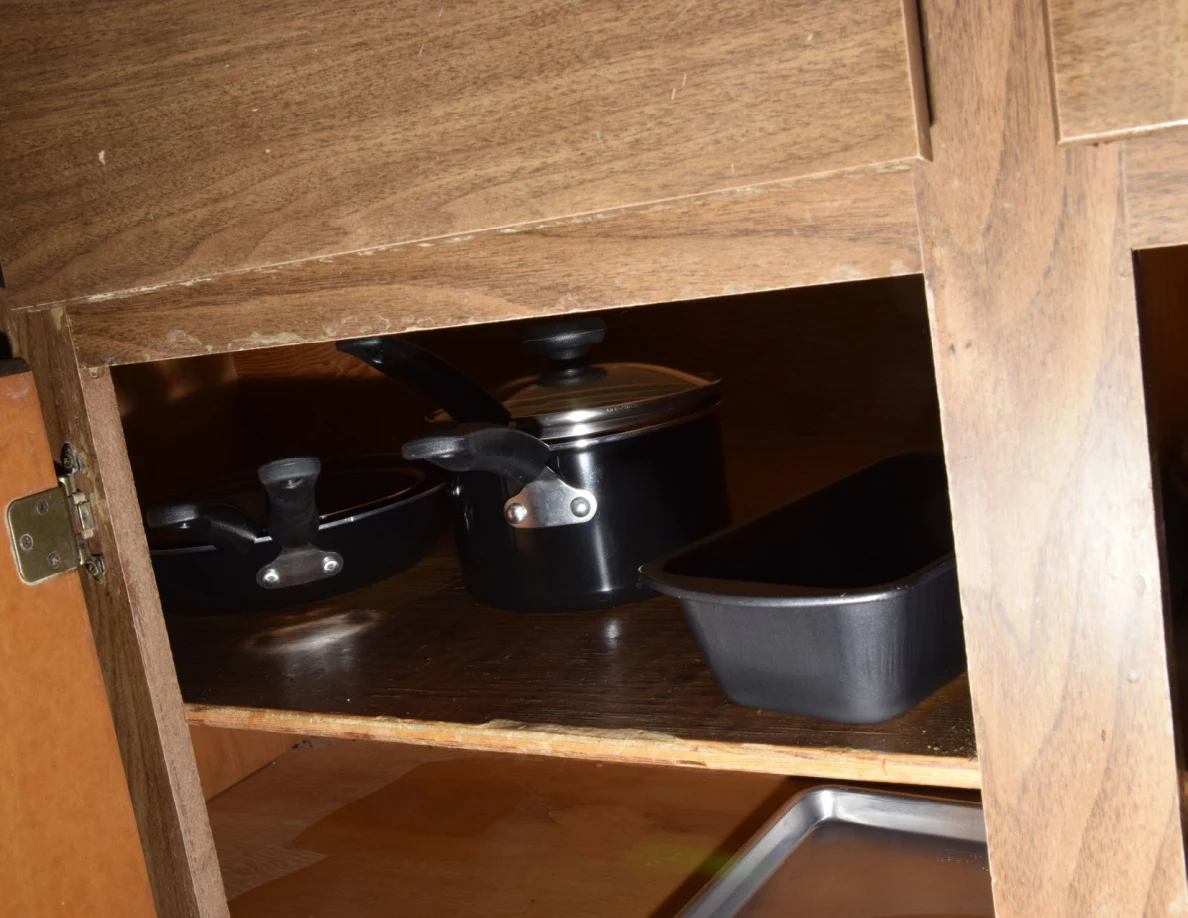 Black lidded pots and a dark baking pan on a wooden cabinet shelf.