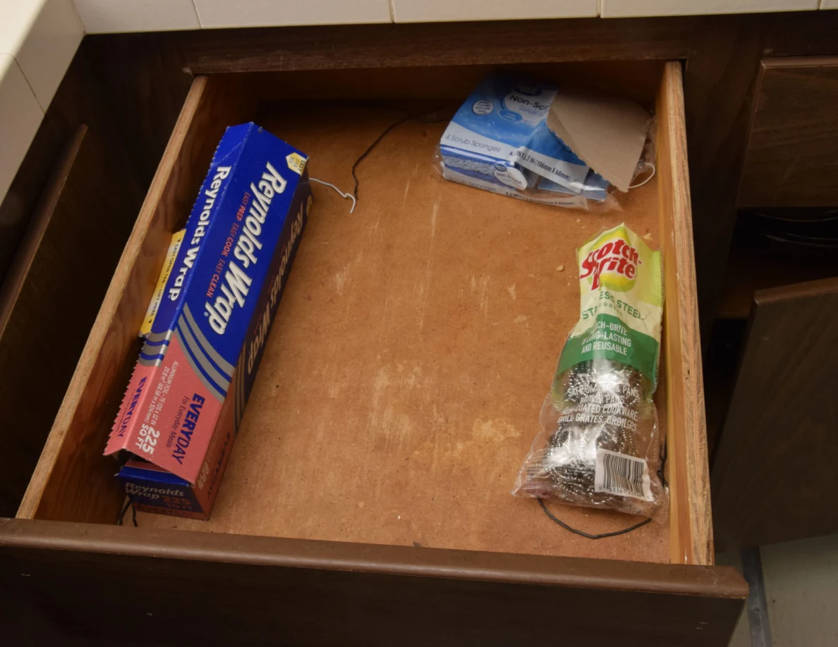 Open kitchen drawer with aluminum foil, a plastic bag and a package of scrubbing pads.