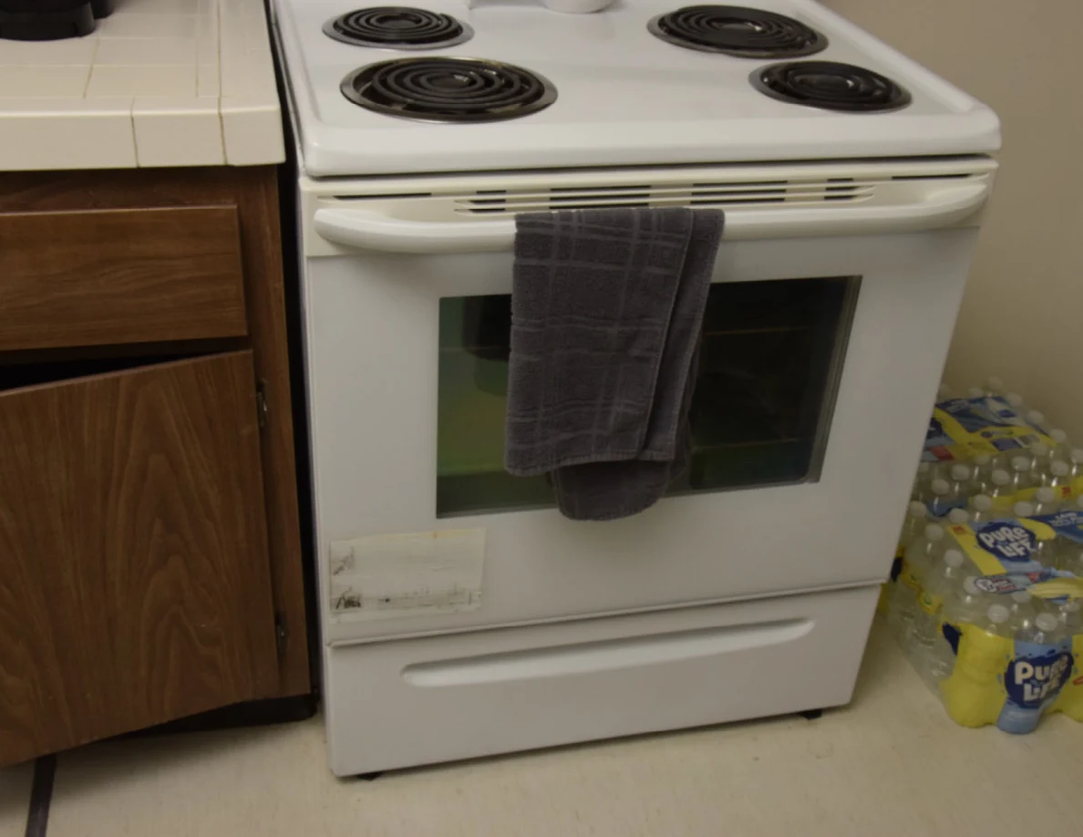 White electric stove and oven with a dark towel hanging from the handle, beside bottled-water packs.