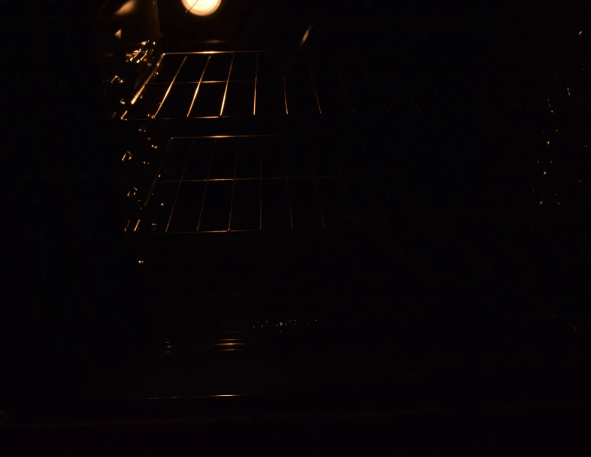 Dark view inside an oven with wire racks faintly lit by the oven light.