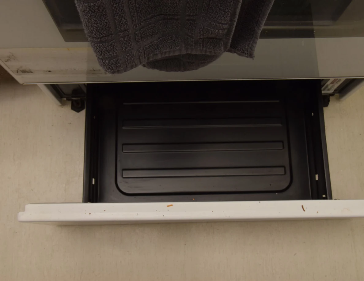 Open lower oven drawer containing a dark ribbed tray.