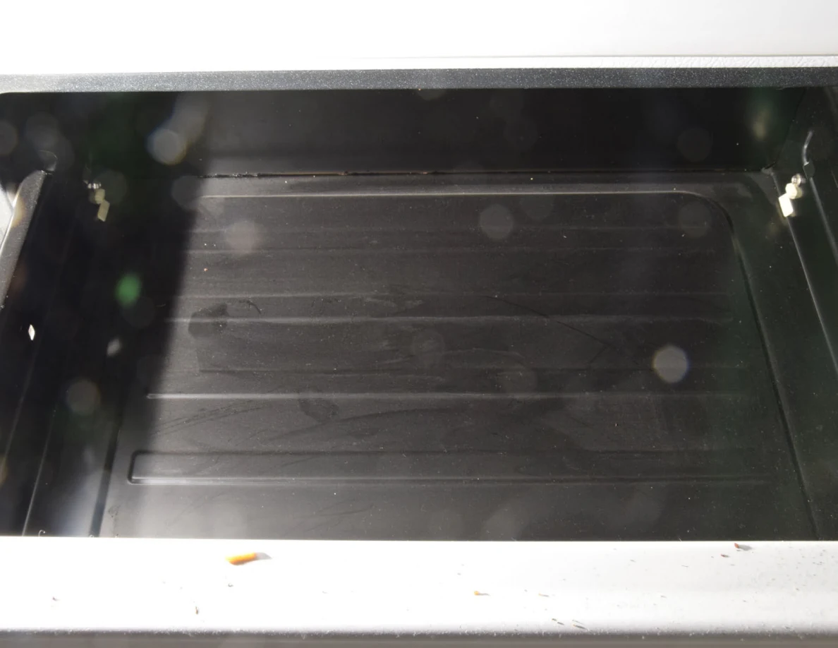 Close view into a dark oven storage drawer with faint streaks across the ribbed base.